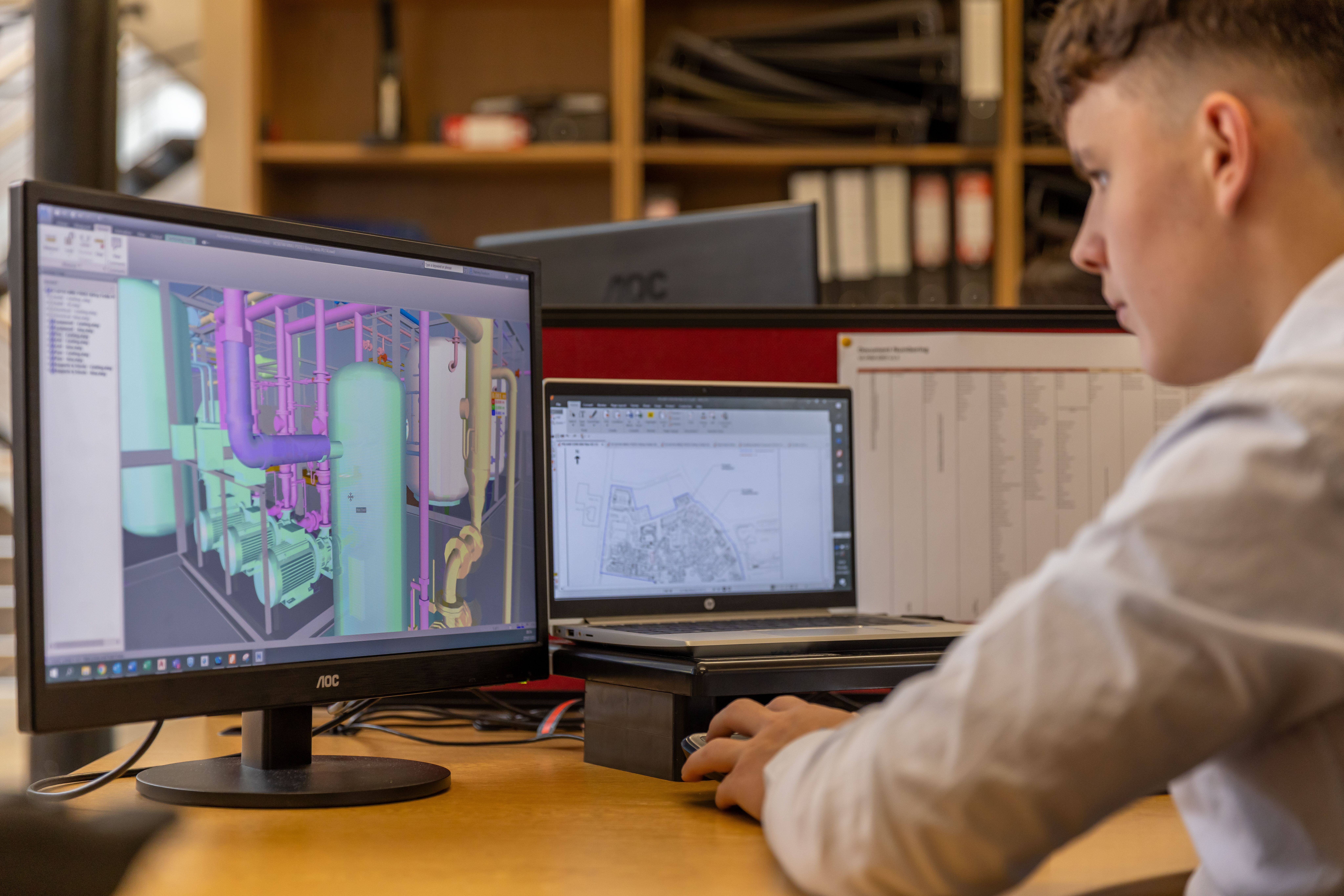 An engineer working across two screens of technical design software.