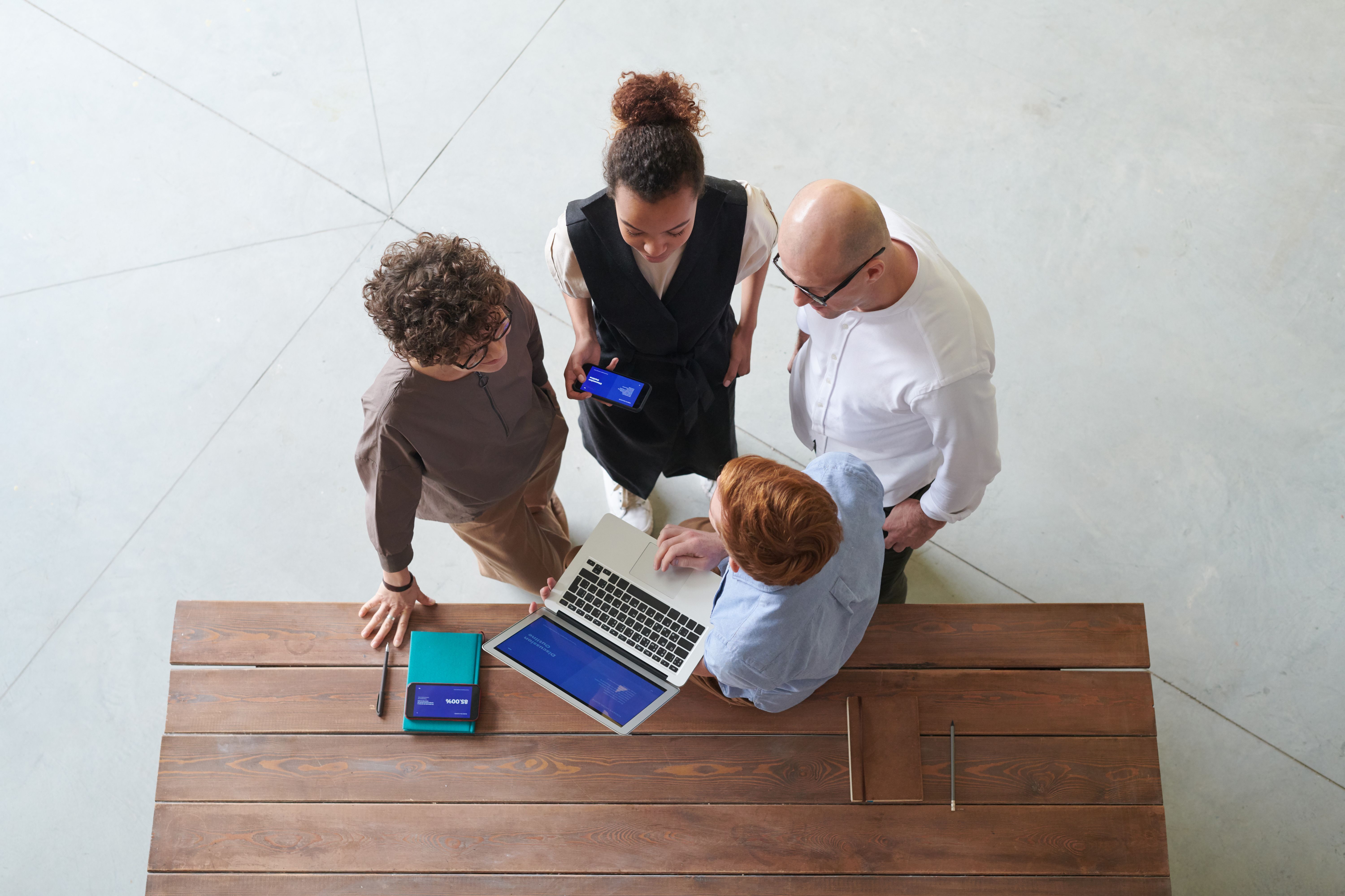 An overhead view of a standing team meeting around a single table.